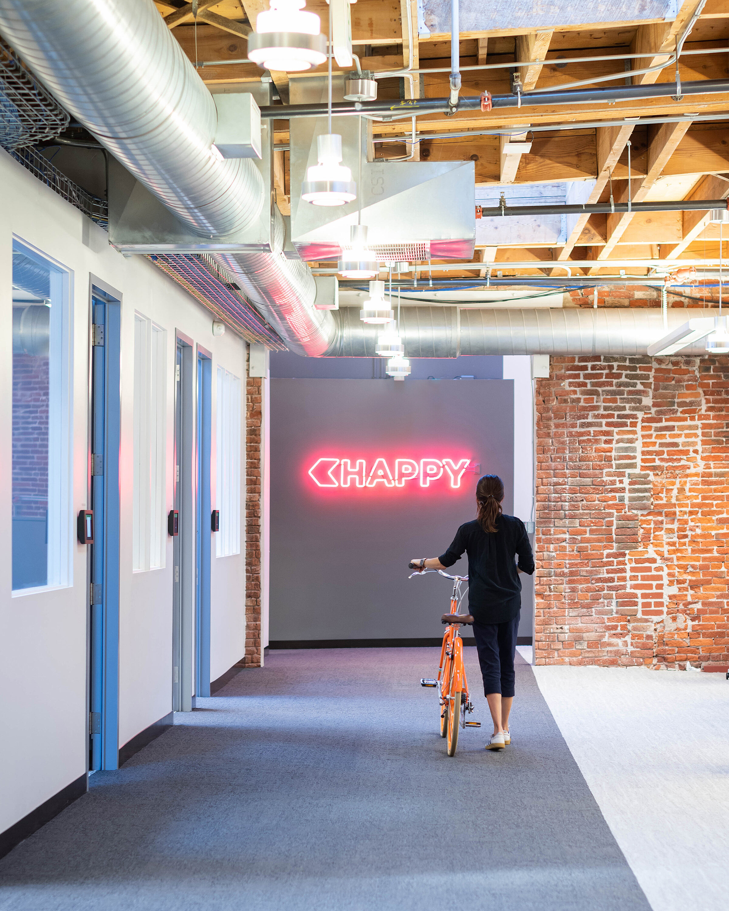 Lady walking bike in office space heading to a lit up Happy sign