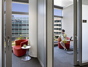 image of two office spaces next to each other. Office on right has a woman on the phone looking out at the window.