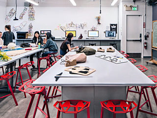 Room looks like a lab with long white tables and red chairs with students working