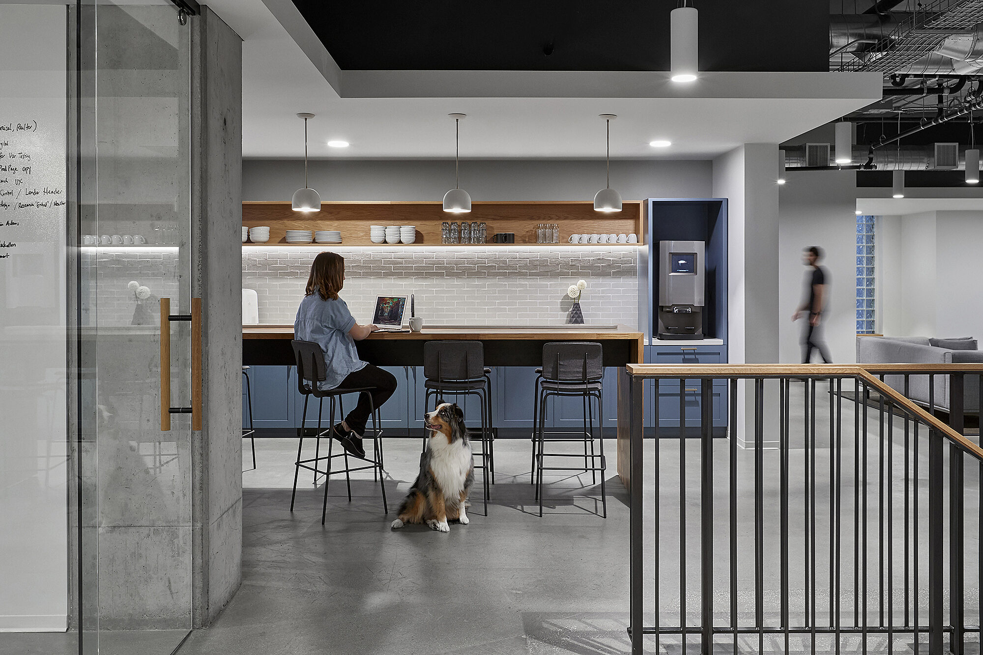 Lady working at high desk in modern workspace with open kitchen
